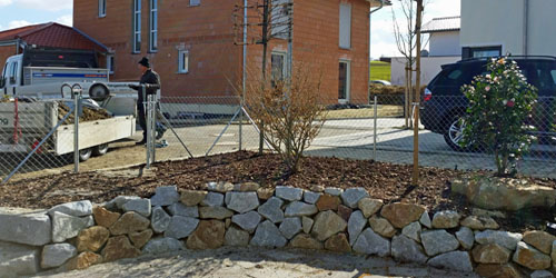 Natursteinmauer in einer Gartenecke mit Bepflanzung